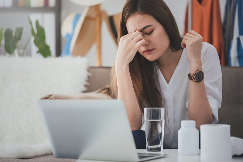 I sintomi da stress lavoro correlato sono rappresentati da una donna davanti ad un pc che porta una mano tra gli occhi per un forte mal di testa